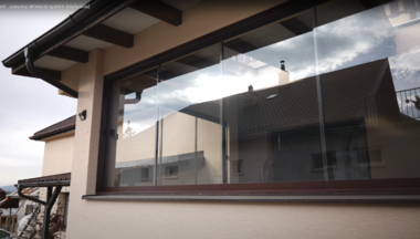 Moderný prístrešok Skyfix pri rodinnom dome, ktorý slúži ako ochrana pre vstup alebo auto, s elegantným dizajnom a pevnou konštrukciou z kovu a skla.